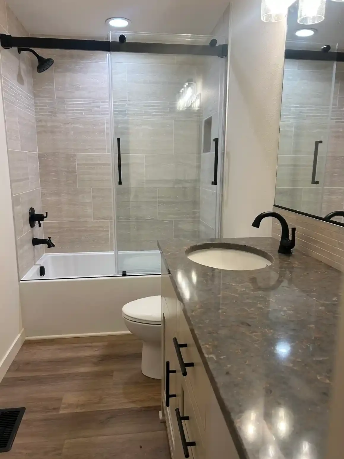 Bathroom with a glass-enclosed tub and shower, gray tile, and a vanity with black fixtures
