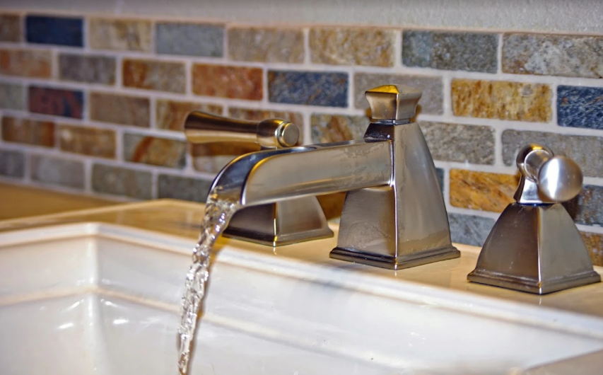 Installed brushed metal bathroom faucet and stone tile backsplash